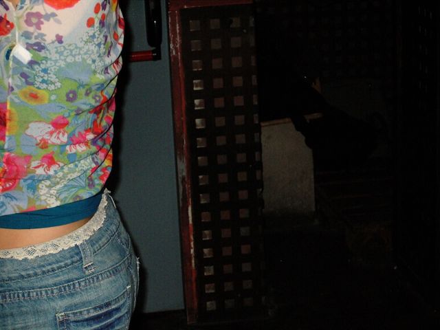 Detalle de una blusa de flores y unos vaqueros con encaje junto a una puerta de madera con celosía
