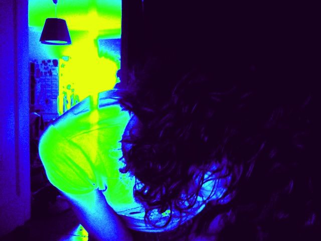 Autorretrato de Roser Amills inclinada, de espaldas, con la melena rizada y un filtro de color azul y amarillo