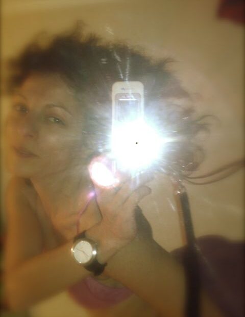 Autorretrato de Roser Amills ante un espejo con el flash del móvil y un reloj en la muñeca