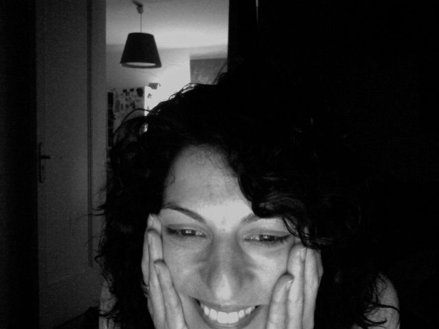 Autorretrato en blanco y negro de Roser Amills sonriendo, con las manos en las mejillas