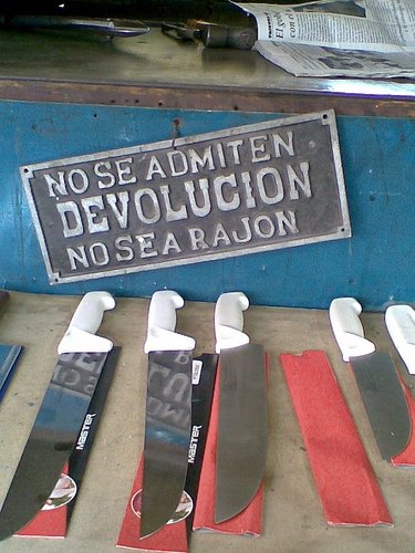Cartel metálico con el texto No se admite devolución, no sea rajón, sobre unos cuchillos de carnicero