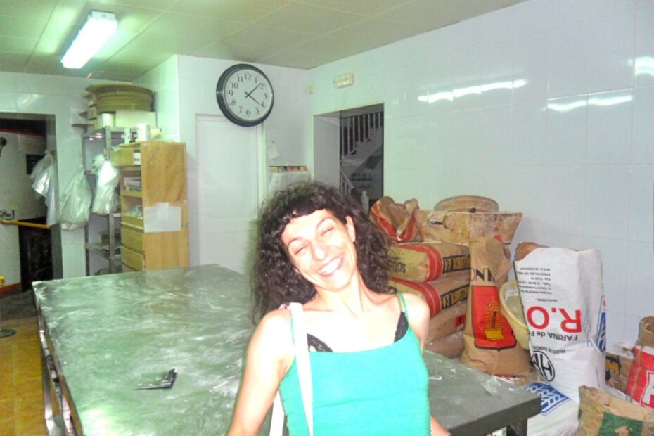 Roser sonriendo con los ojos cerrados en el obrador, junto a una mesa de acero y sacos de harina