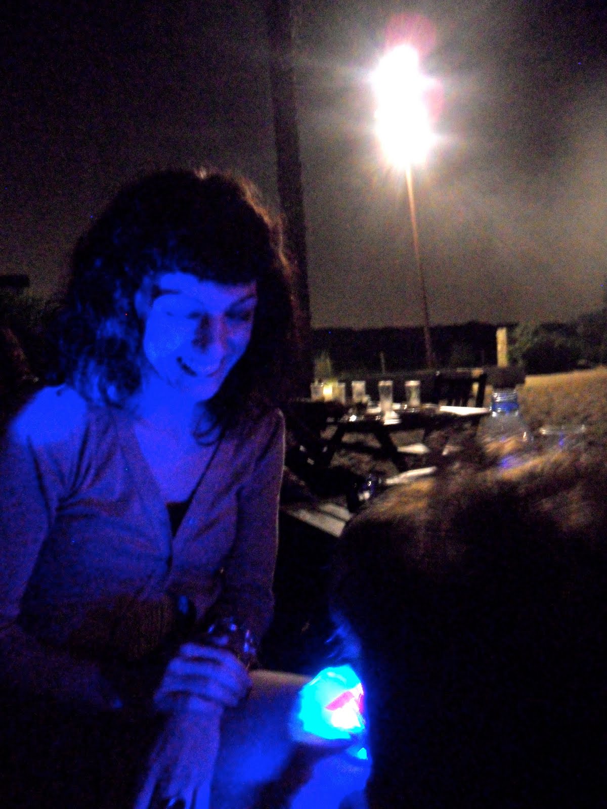 Mujer sonriente de noche con una luz azul en primer plano, en la Erotic Soirée de la playa del Prat
