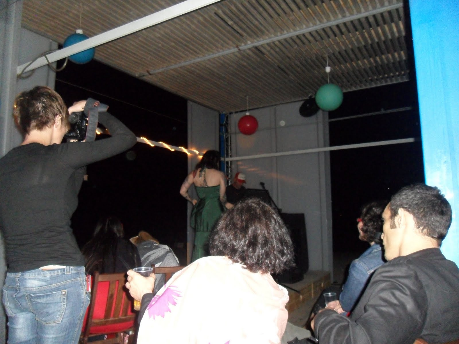 Público y una fotógrafa durante el recital; al fondo, una persona de pie en el escenario bajo globos