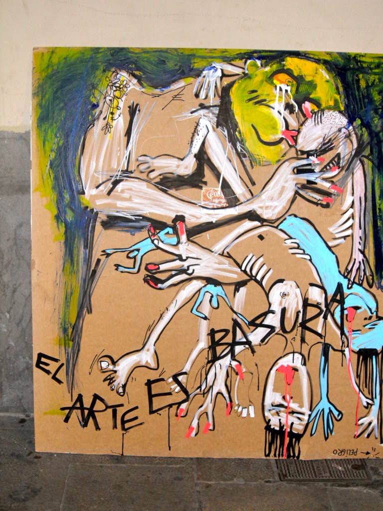 Cartón pintado apoyado en una pared con figuras blancas y azules sobre un fondo verde y la leyenda «El arte es basura»