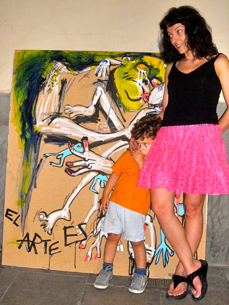 Roser Amills, con top negro y falda rosa, mira hacia un lado mientras un niño se tapa la cara a su lado, delante de la obra «El arte es basura»