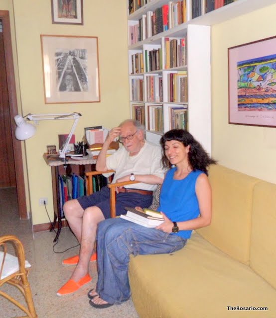 Roser Amills, amb vestit blau, asseguda en un sofà groc amb llibres, al costat de Cristóbal Serra