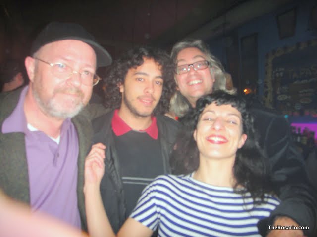 Roser Amills, amb jersei de ratlles, amb un home amb barret, un jove arrissat i una dona amb ulleres en un local fosc
