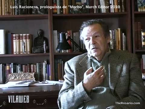 Luis Racionero, assegut davant d'una prestatgeria plena de llibres, parla amb la mà al pit