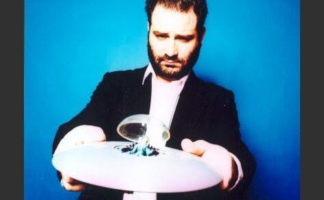 Óscar Aibar sosté amb les dues mans un plat blanc amb una petita escultura de vidre, sobre un fons blau