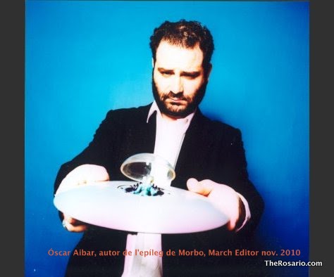 Óscar Aibar sosté amb les dues mans un plat blanc amb una petita escultura de vidre, sobre un fons blau