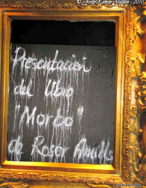 Pissarra amb marc daurat on es llegeix, escrit amb guix, «Presentación del libro «Morbo» de Roser Amills»