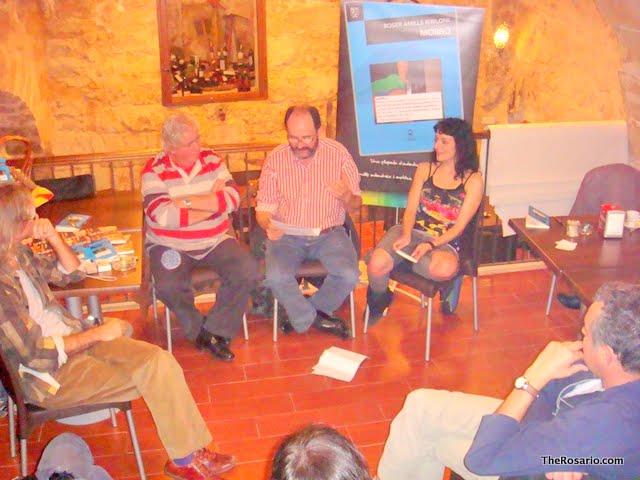 Persones assegudes en rotllana durant la presentació de Morbo a Vall-de-Roures, amb un cartell del llibre al fons