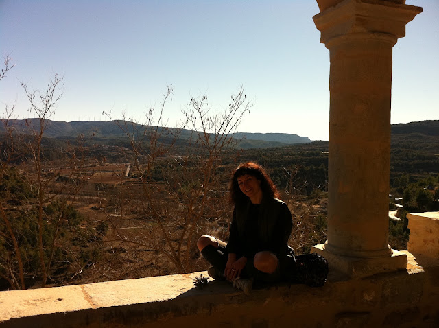 Una dona asseguda en una cornisa de pedra, a contrallum, davant d'un paisatge de muntanya