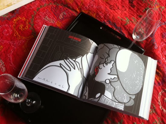 Exemplar de «Paraules d'amor» obert sobre una tela vermella, amb una il·lustració a doble pàgina i copes de vi al costat
