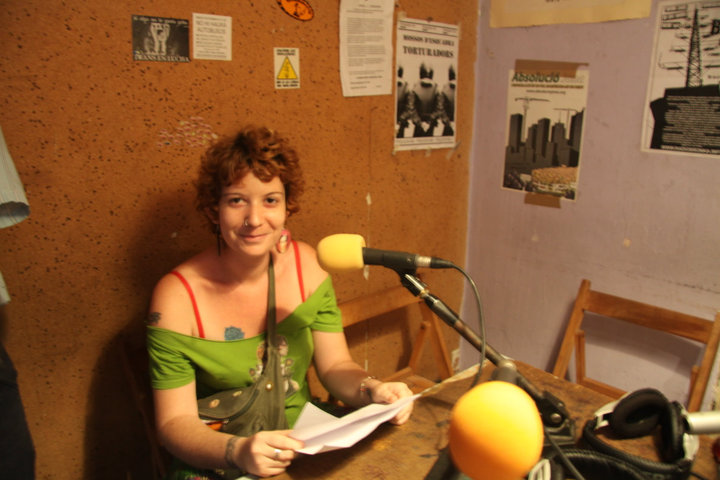 Princesa Inca, de cabell arrissat i curt, somrient, davant d'un micròfon en un estudi de ràdio amb un full a la mà