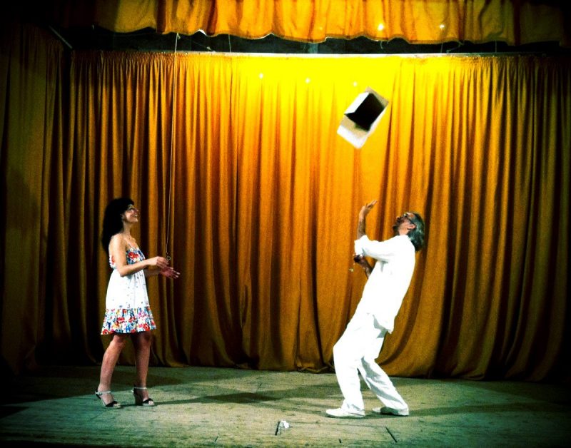 Víctor Amela, vestido de blanco, lanza un libro al aire ante Roser Amills en un escenario con telón dorado
