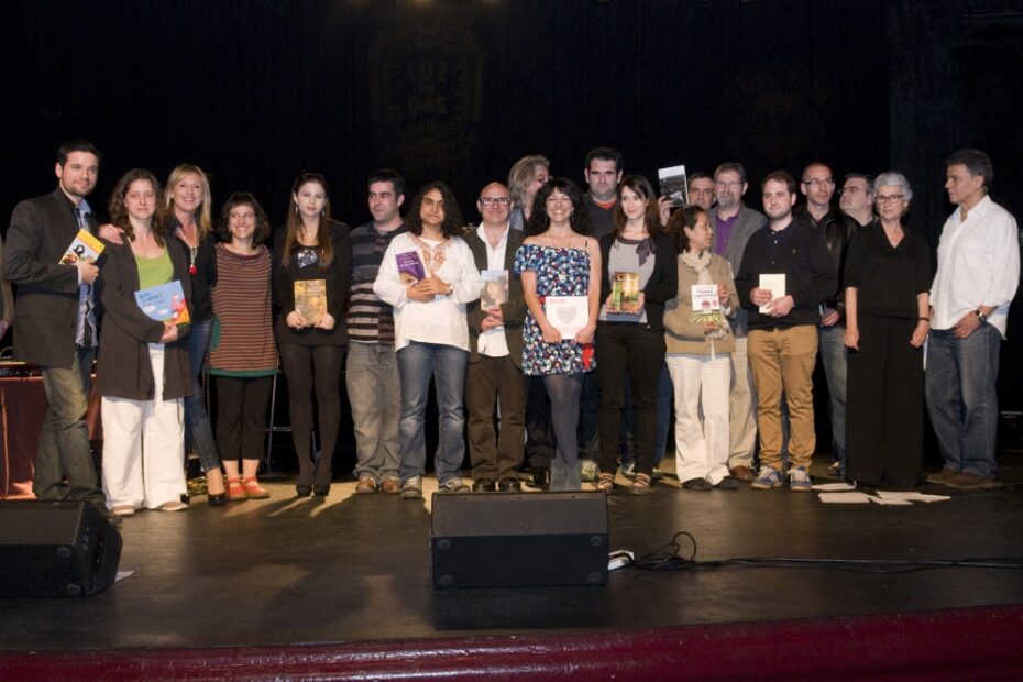 Foto de grup d'una vintena de persones dretes a l'escenari d'un teatre, moltes amb un llibre a les mans