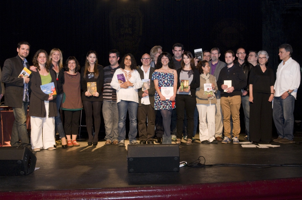 Foto de grup d'una vintena de persones dretes a l'escenari d'un teatre, moltes amb un llibre a les mans