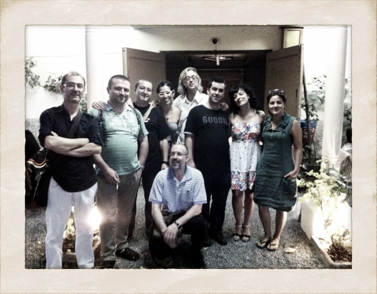 Un grup d'homes i dones posen dretes i asseguts en un pati davant la porta oberta d'un edifici, en una foto amb marc antic