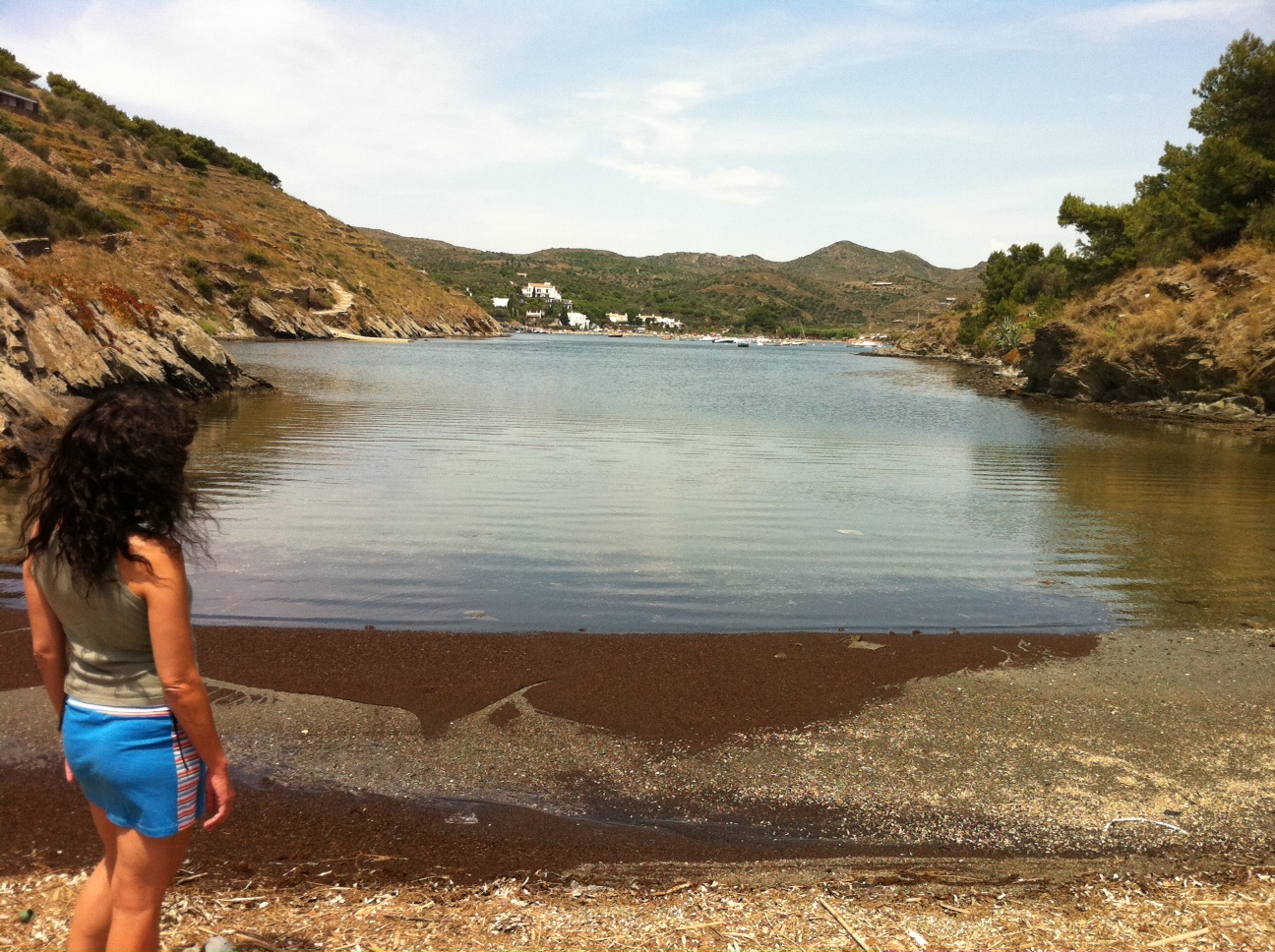 Una dona de cabells arrissats mira una cala tranquil·la de Portlligat envoltada de vegetació