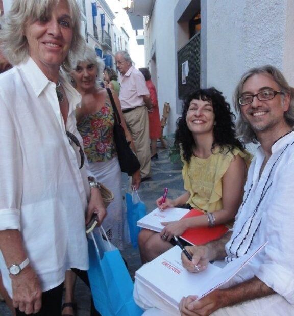 Roser Amills i Víctor Amela signant llibres al carrer, a Cadaqués, amb dues lectores dretes al davant