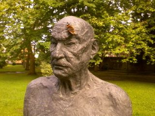 Bust de bronze d'un home gran en un parc, amb una papallona sobre el front