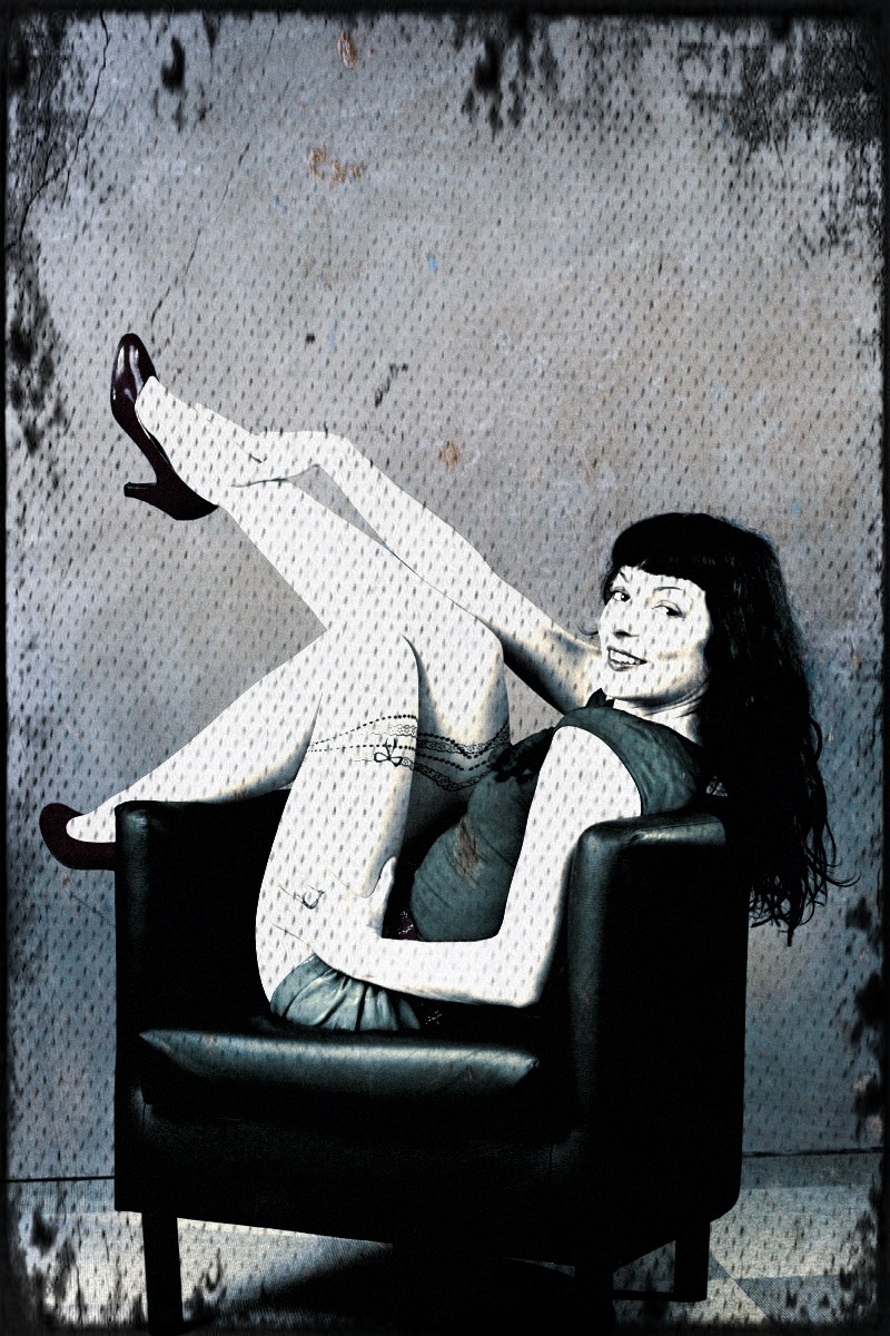 Roser Amills sentada en una butaca negra con las piernas en alto, en una fotografía en blanco y negro con textura de pared vieja