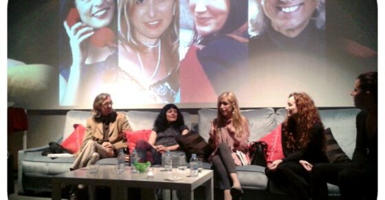 Quatre autors i una persona més asseguts en sofàs davant d'una projecció amb els seus retrats, durant el sopar-tertúlia del Kubb d'Igualada