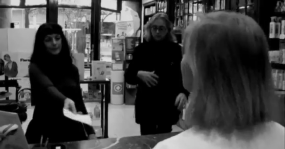 Dins la farmàcia, Roser Amills allarga un paper mentre Víctor Amela, amb ulleres, és al seu costat i, en primer terme, una dona de cabell curt els dona l'esquena