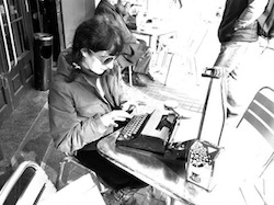 Roser Amills escribiendo a máquina sentada a una mesa de terraza, foto en blanco y negro