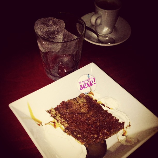 Pin de «M'agrada el sexe» sobre un trozo de tarta de chocolate, junto a un café y un vaso de agua