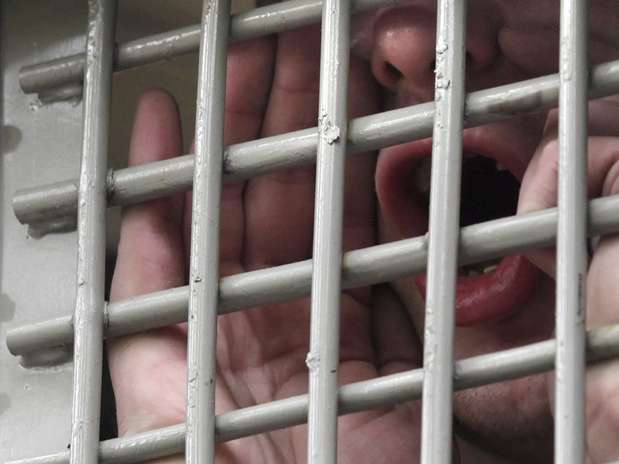 Una mano abierta tras unos barrotes grises y, al fondo, una boca que grita