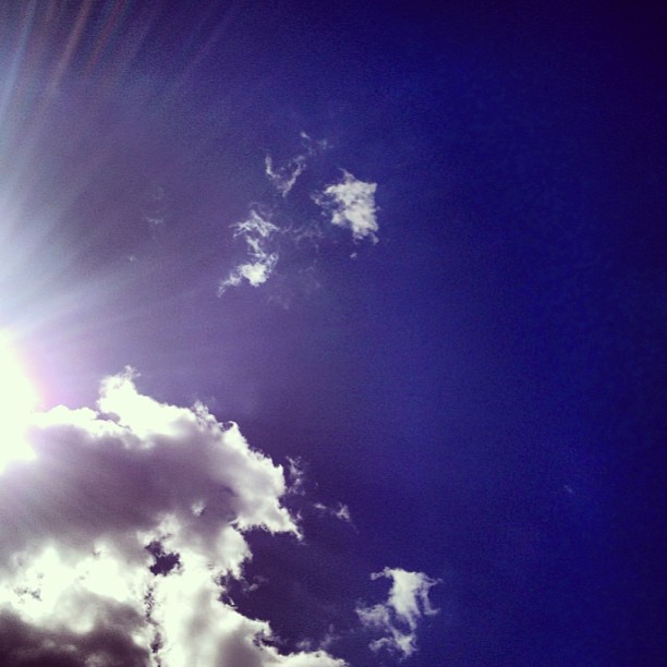 Cielo azul con nubes blancas y el sol asomando por un lado