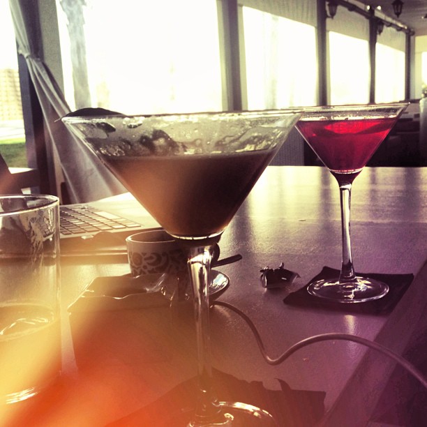 Dos copas de cóctel, una de chocolate y otra roja, sobre una mesa junto a un portátil