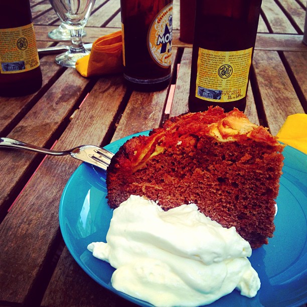 Trozo de bizcocho de chocolate con nata y botellas de cerveza sobre una mesa de madera