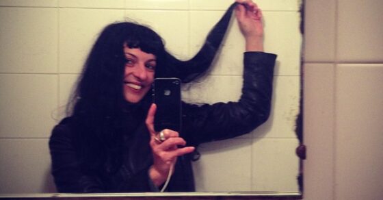 Roser Amills con una mano en el pelo, haciéndose un selfi en el espejo de un lavabo con azulejos