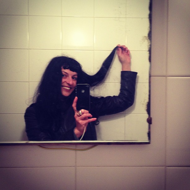 Roser Amills con una mano en el pelo, haciéndose un selfi en el espejo de un lavabo con azulejos