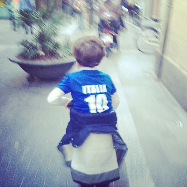 Niño de espaldas con la camiseta azul de Italia número 10 corriendo por una calle