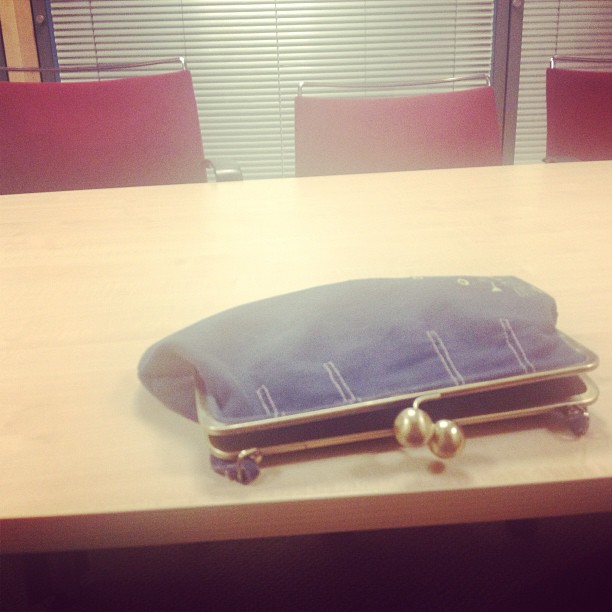 Bolso azul con cierre de bolas de perla abierto sobre una mesa de reunión
