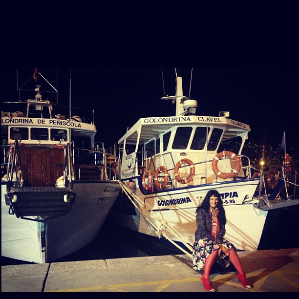 Roser Amills sentada en el puerto de Peñíscola, entre dos barcos de pesca por la noche