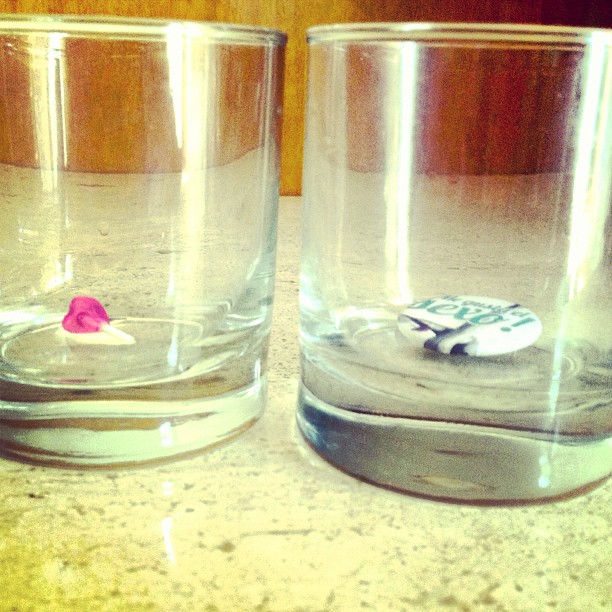Dos vasos vacíos sobre una mesa, con una chapa de ¡Me gusta el sexo! en el fondo de uno
