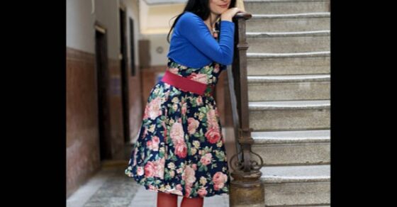 Roser Amills apoyada en la barandilla de una escalera, con vestido de flores y medias rojas