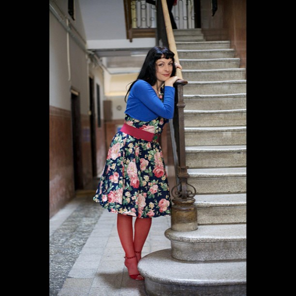 Roser Amills apoyada en la barandilla de una escalera, con vestido de flores y medias rojas