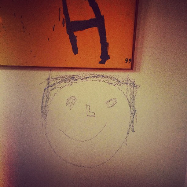 Dibujo a lápiz de una cara sonriente en la pared, bajo un cuadro