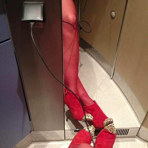 Pierna con media roja y zapatos rojos de tachuelas junto a un enchufe en un lavabo del AVE