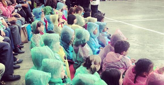 Niños con chubasqueros de colores sentados en el patio de un colegio durante un festival