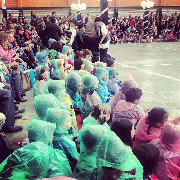 Niños con chubasqueros de colores sentados en el patio de un colegio durante un festival