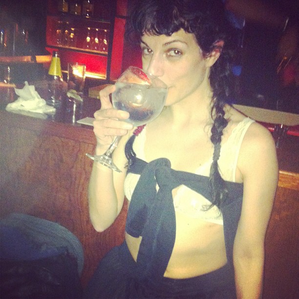 Roser Amills bebiendo de una copa en un bar, con trenza y top oscuro