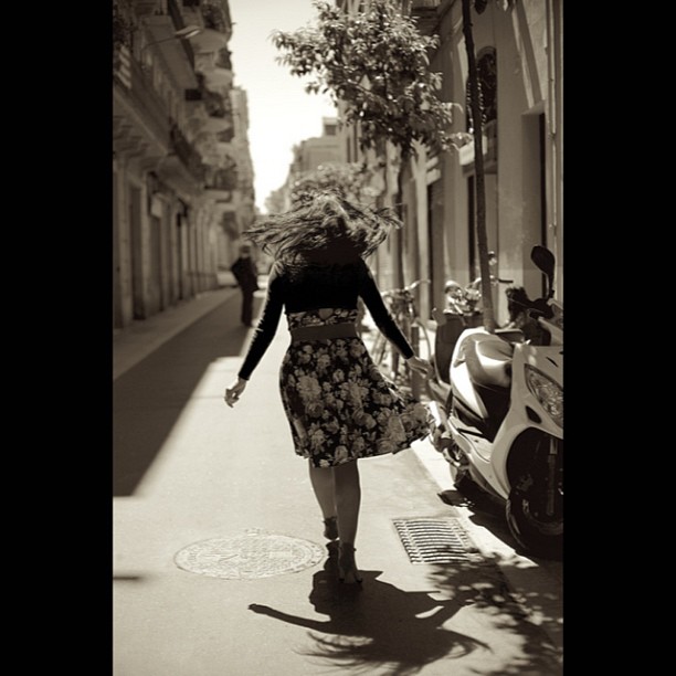 Roser Amills de espaldas, con el pelo al viento, caminando por una calle de Barcelona en blanco y negro